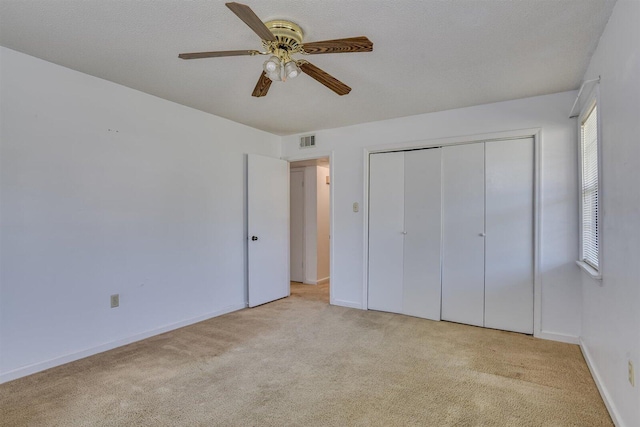 unfurnished bedroom with a textured ceiling, ceiling fan, light carpet, and a closet