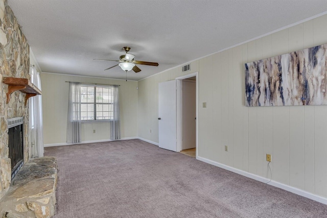 unfurnished living room featuring light carpet, a textured ceiling, ceiling fan, crown molding, and a stone fireplace