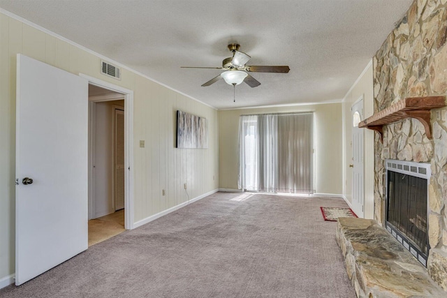 unfurnished living room featuring light colored carpet, a stone fireplace, ceiling fan, and crown molding