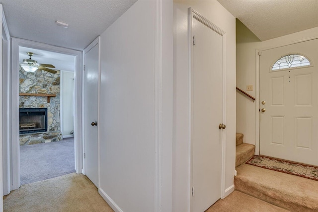 foyer featuring a stone fireplace, light carpet, ceiling fan, and a textured ceiling