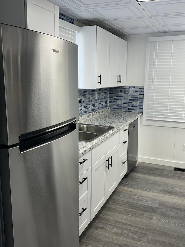 kitchen with appliances with stainless steel finishes, tasteful backsplash, light stone counters, white cabinets, and dark hardwood / wood-style floors