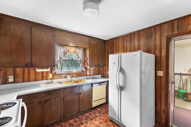 kitchen featuring sink, white appliances, wooden walls, dark brown cabinetry, and a textured ceiling