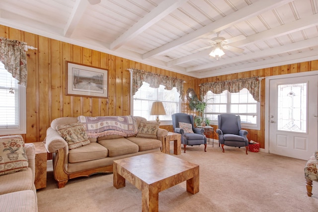 carpeted living room with ceiling fan, beam ceiling, and wooden walls