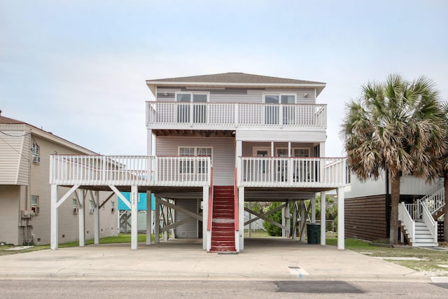 beach home with a carport, a balcony, concrete driveway, a shingled roof, and stairs