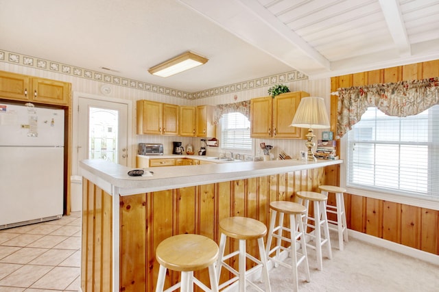 kitchen featuring light countertops, a sink, beamed ceiling, freestanding refrigerator, and a peninsula