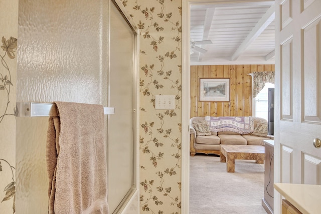 full bath featuring a shower with door, ceiling fan, beam ceiling, and wooden walls