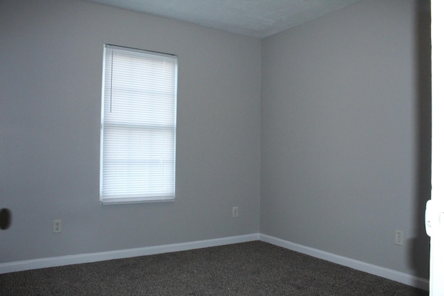 spare room with dark carpet and baseboards