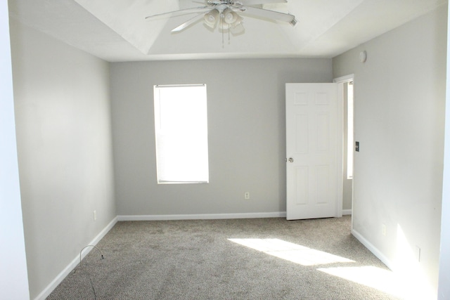 carpeted empty room with a raised ceiling, ceiling fan, and baseboards