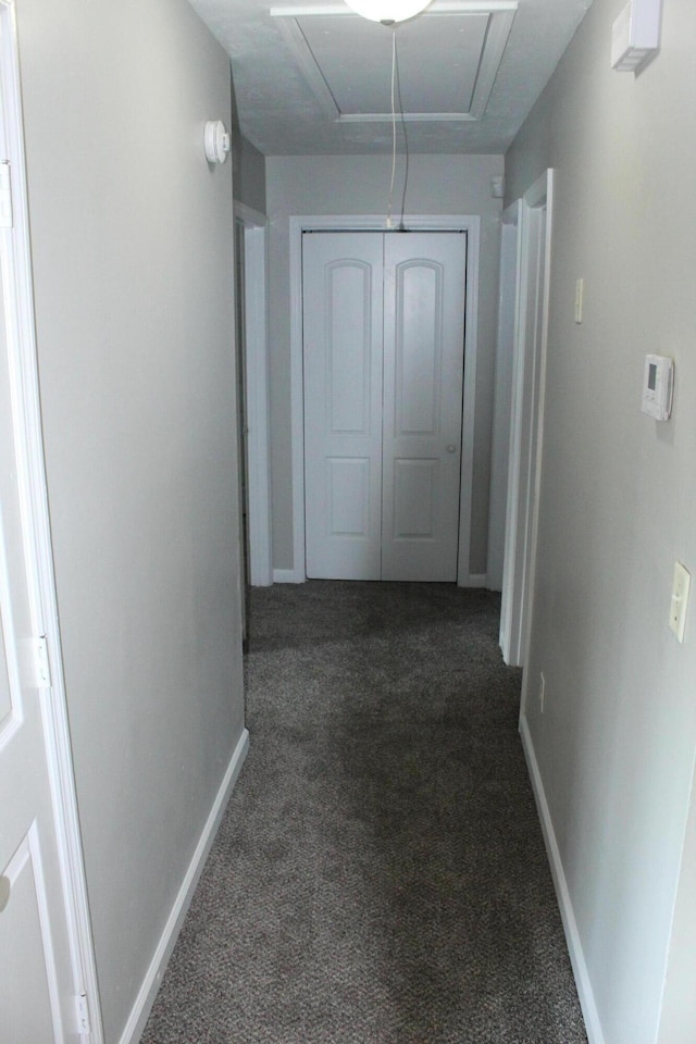 corridor featuring dark carpet, baseboards, and attic access