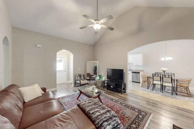 living area featuring arched walkways, a ceiling fan, light wood-style floors, a chandelier, and baseboards
