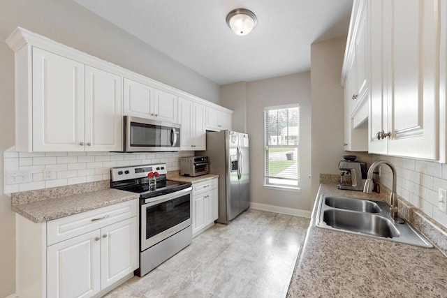kitchen with stainless steel appliances, a sink, decorative backsplash, and white cabinetry
