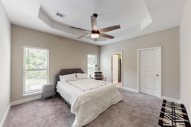 carpeted bedroom featuring a raised ceiling, multiple windows, and baseboards