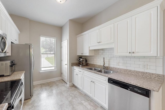 kitchen featuring stainless steel appliances, a sink, backsplash, white cabinets, and baseboards