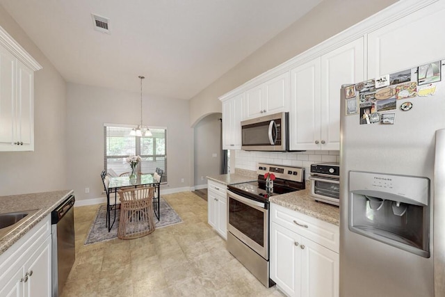 kitchen with appliances with stainless steel finishes, arched walkways, white cabinets, decorative backsplash, and baseboards
