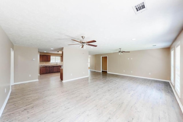 unfurnished living room featuring ceiling fan, a healthy amount of sunlight, and light wood-type flooring