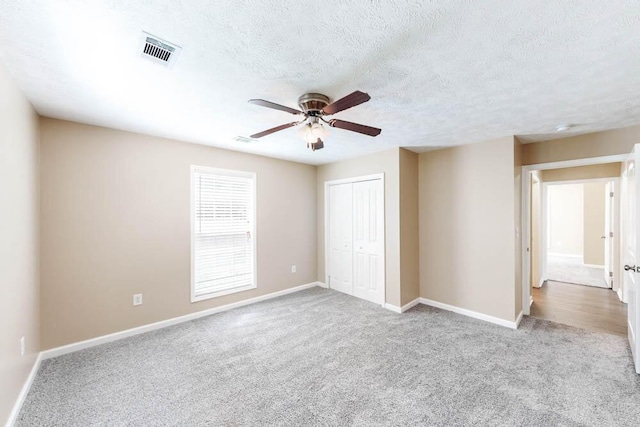 unfurnished bedroom with a textured ceiling, a closet, ceiling fan, and light colored carpet