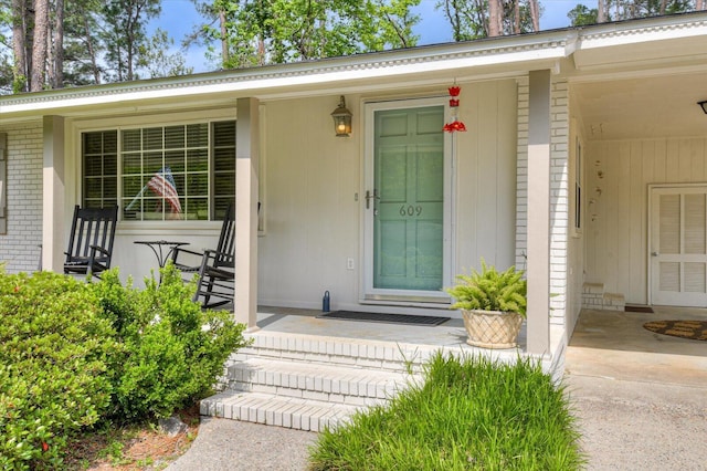 doorway to property featuring a porch and brick siding