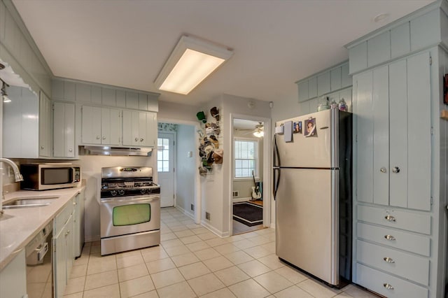 kitchen featuring ceiling fan, appliances with stainless steel finishes, a sink, light tile patterned floors, and under cabinet range hood