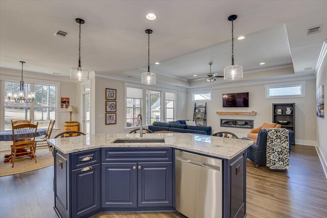 kitchen featuring ceiling fan with notable chandelier, sink, stainless steel dishwasher, an island with sink, and a tray ceiling