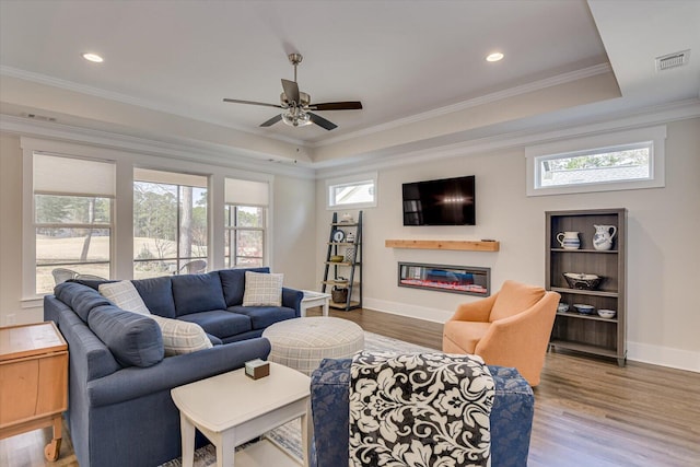 living room featuring a raised ceiling, ceiling fan, hardwood / wood-style floors, and ornamental molding