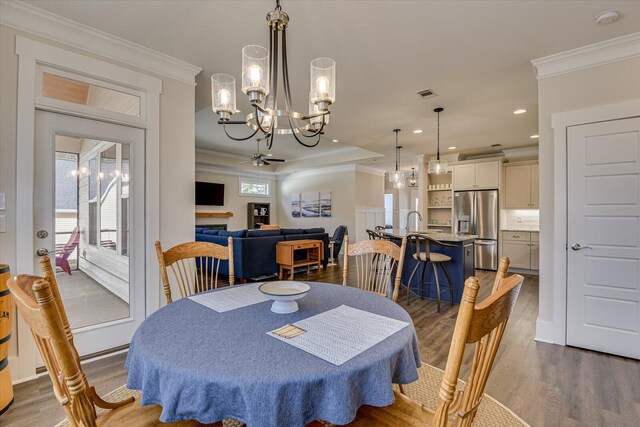 dining area featuring ceiling fan with notable chandelier, sink, crown molding, and dark wood-type flooring