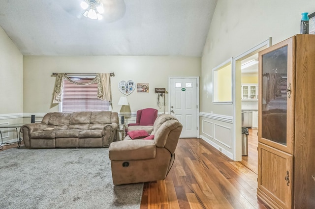 living room with wood-type flooring, a ceiling fan, vaulted ceiling, and a wainscoted wall
