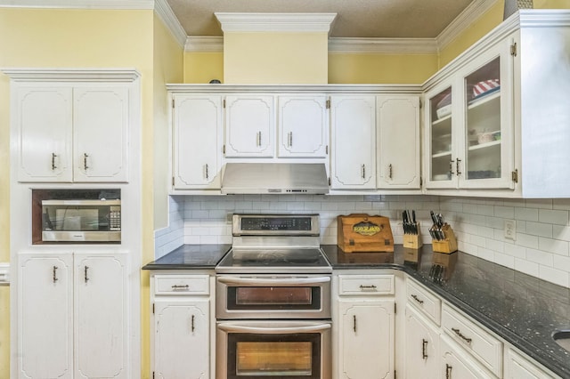 kitchen with appliances with stainless steel finishes, exhaust hood, dark countertops, ornamental molding, and glass insert cabinets