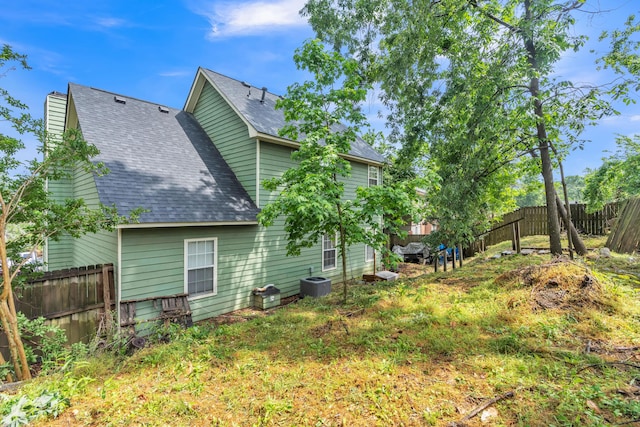 rear view of property featuring roof with shingles, cooling unit, a fenced backyard, and a chimney