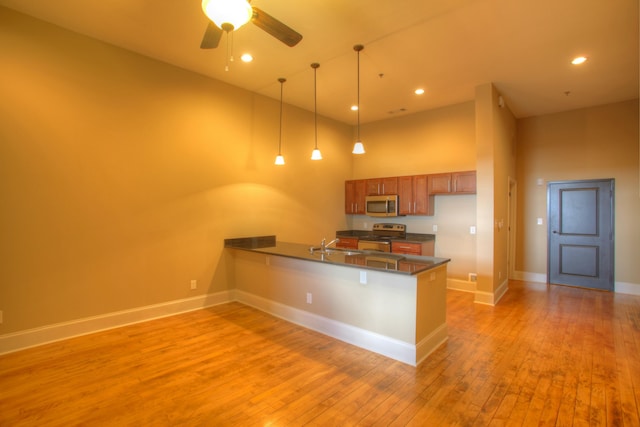 kitchen with light wood-type flooring, kitchen peninsula, pendant lighting, a towering ceiling, and stainless steel appliances