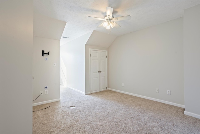 interior space with carpet, baseboards, ceiling fan, vaulted ceiling, and a textured ceiling