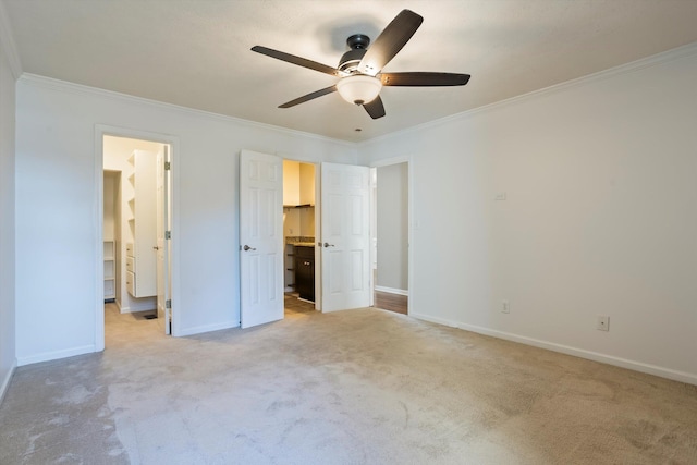 unfurnished bedroom with a spacious closet, crown molding, baseboards, ceiling fan, and light colored carpet