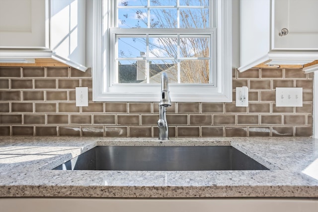 kitchen featuring a sink, decorative backsplash, and light stone countertops