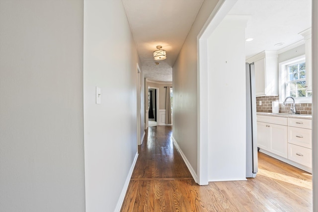 hallway featuring light wood-style flooring, baseboards, and a sink