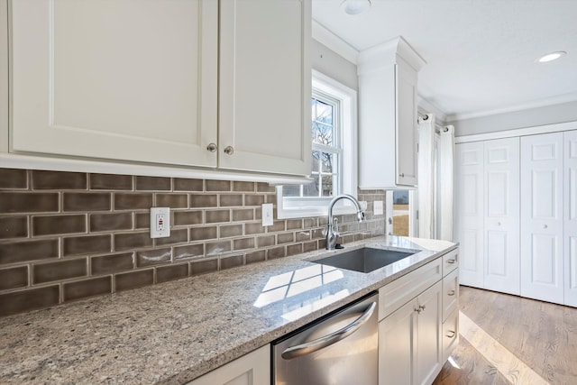 kitchen with light stone counters, a sink, white cabinets, stainless steel dishwasher, and tasteful backsplash