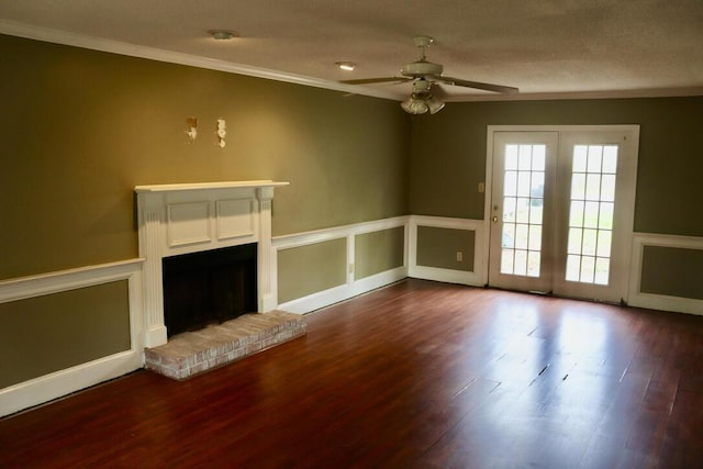 unfurnished living room with crown molding, a brick fireplace, ceiling fan, dark wood-style floors, and a wainscoted wall
