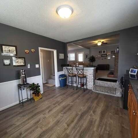 kitchen featuring dark countertops, a wainscoted wall, brown cabinets, wood finished floors, and a textured ceiling