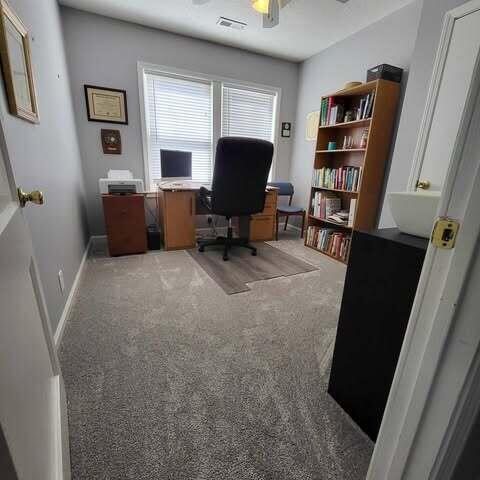 carpeted office featuring visible vents, baseboards, and a ceiling fan