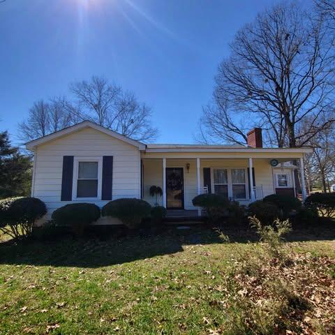 view of front facade with a front lawn, a porch, and a chimney