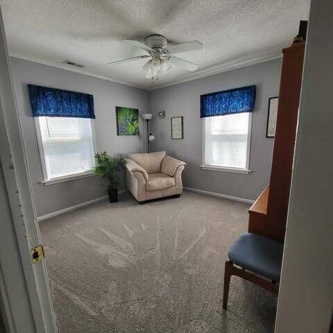 living area featuring a ceiling fan, visible vents, carpet floors, and a textured ceiling