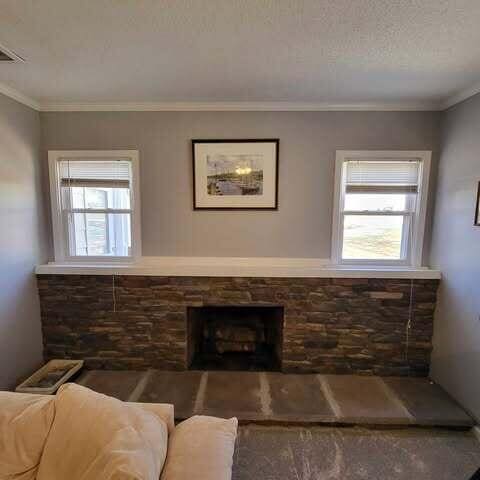 living room with a textured ceiling, a stone fireplace, and ornamental molding