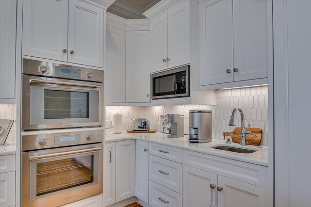 kitchen with light stone counters, a sink, white cabinets, appliances with stainless steel finishes, and decorative backsplash