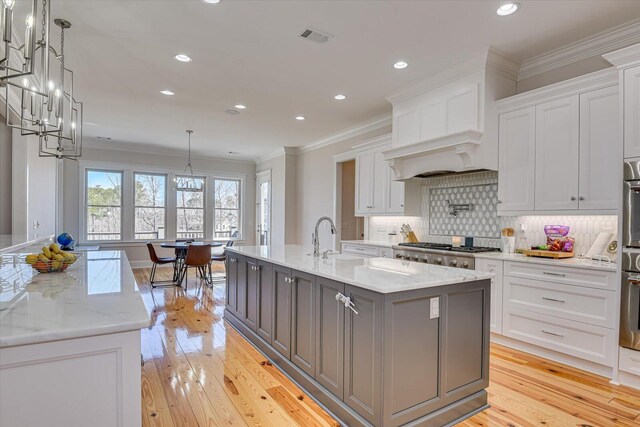 kitchen featuring tasteful backsplash, visible vents, ornamental molding, a kitchen island with sink, and white cabinetry