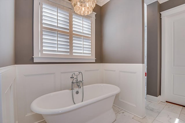 full bath featuring marble finish floor, an inviting chandelier, a wainscoted wall, and a soaking tub