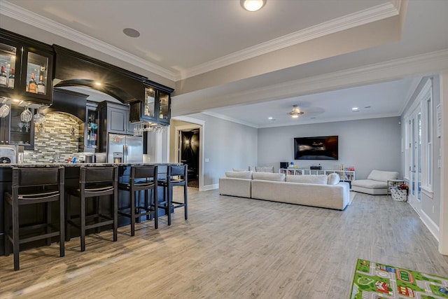 living room featuring light wood-type flooring, baseboards, wet bar, and ornamental molding