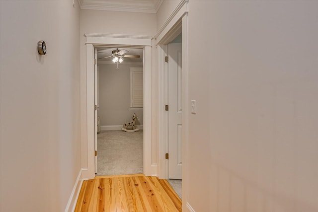 hall with ornamental molding, baseboards, and light wood finished floors