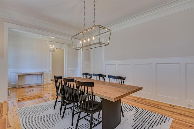 dining area featuring ornamental molding, a decorative wall, and light wood finished floors