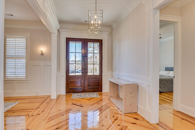 entrance foyer with visible vents, ornamental molding, a decorative wall, and french doors