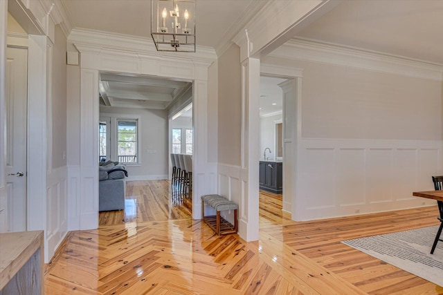 hall featuring ornamental molding, wainscoting, a notable chandelier, and parquet floors