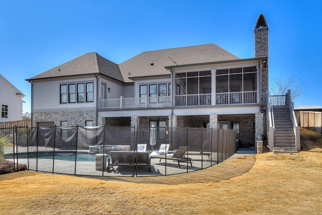 back of property with a patio, a sunroom, stone siding, a lawn, and stairway