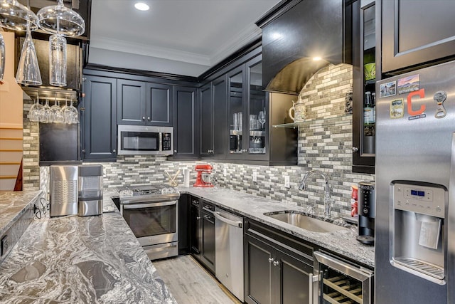 kitchen featuring light stone counters, beverage cooler, stainless steel appliances, a sink, and crown molding